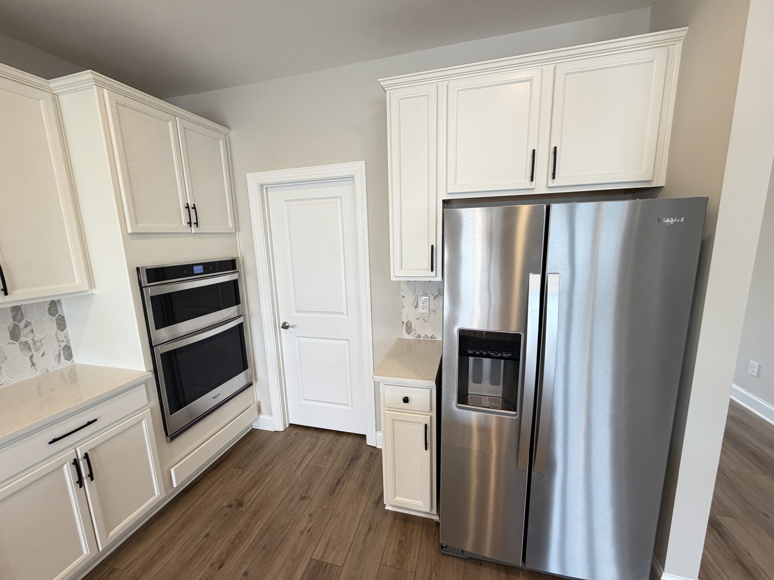 Modern kitchen with white shaker cabinets, light countertops, and a stainless steel French‑door refrigerator with an ice dispenser.