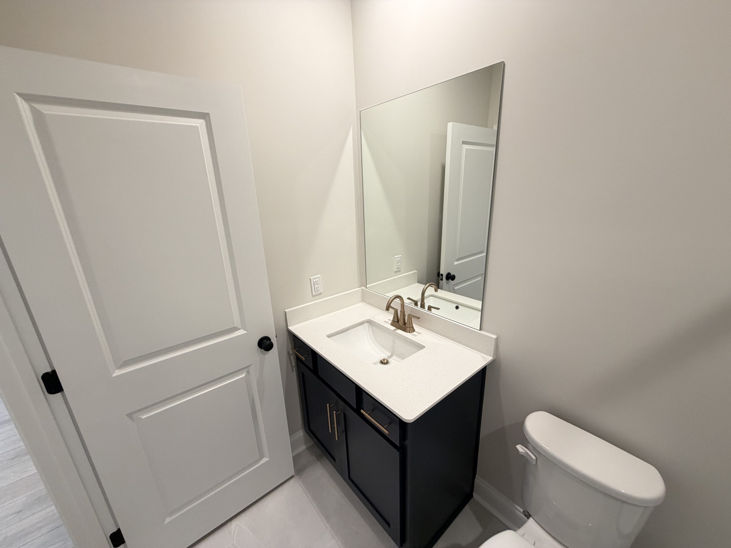 Modern bathroom with a white countertop sink, dark vanity, brass faucet, and a large rectangular mirror above the sink.