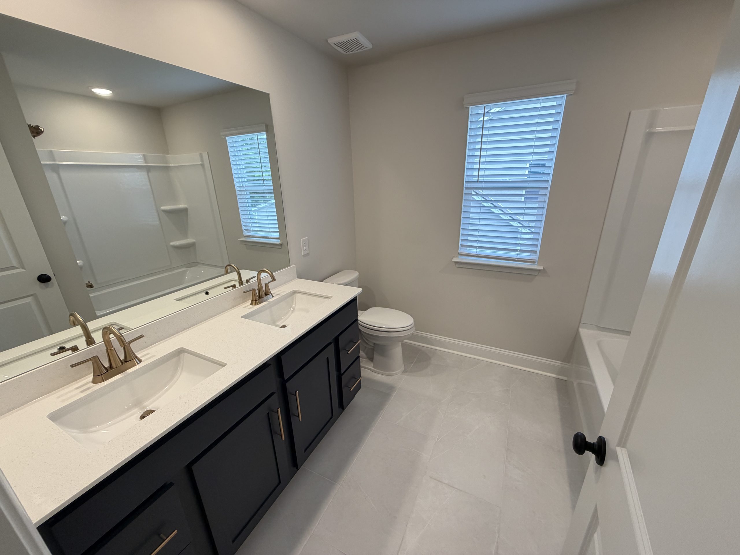Modern bathroom with a double-sink vanity, dark cabinets, brass faucets, large mirror, and a tub–shower combo.