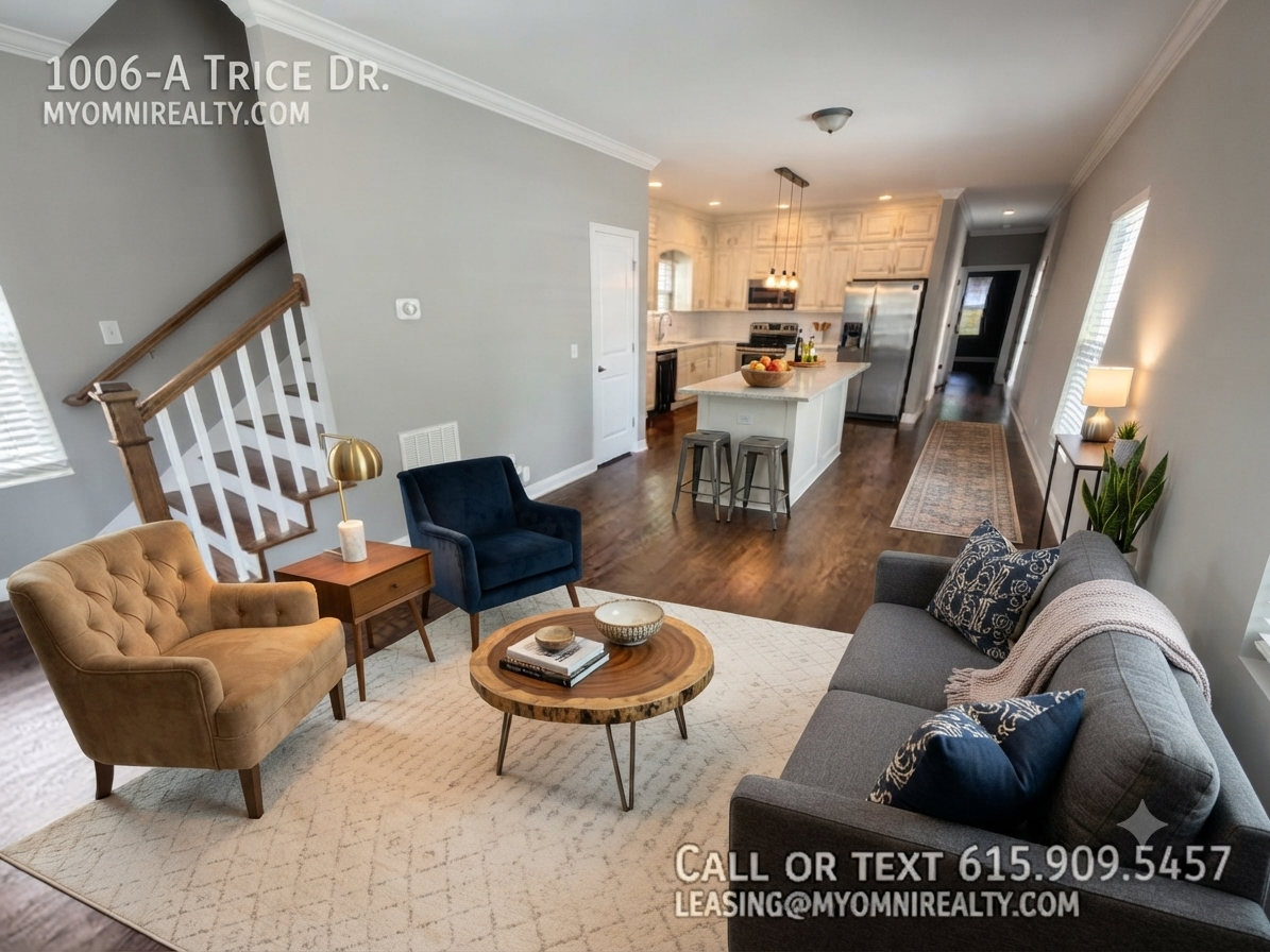 Open-concept living room with gray walls, beige armchairs, a blue accent chair, a rustic coffee table, and a kitchen island in the background.