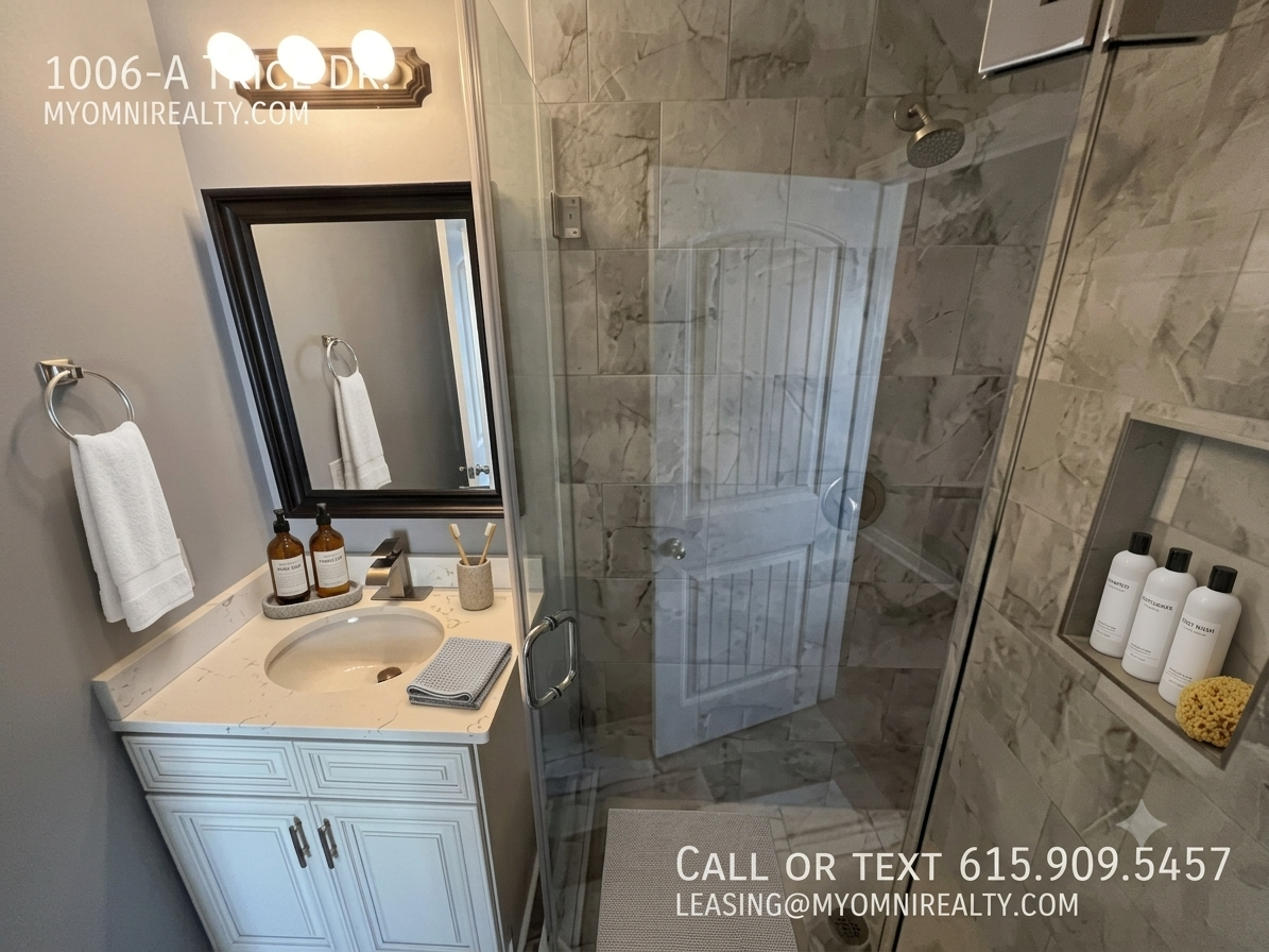 Bathroom vanity with marble countertop, sink, and mirror, towels hanging nearby and a glass-enclosed shower; rental contact info overlaid on the image.