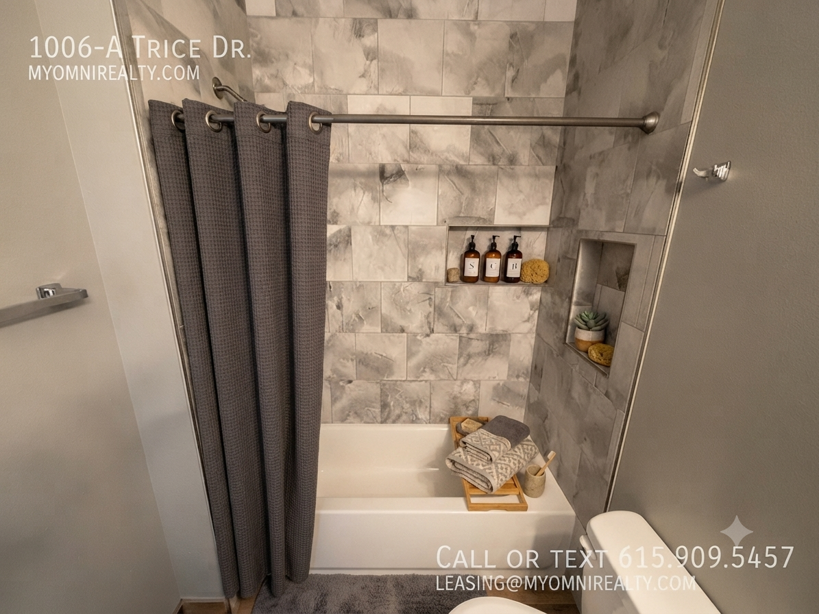 Modern marble-tiled bathroom with a white tub, dark gray shower curtain, built-in niche holding bottles, and a wooden bath tray.