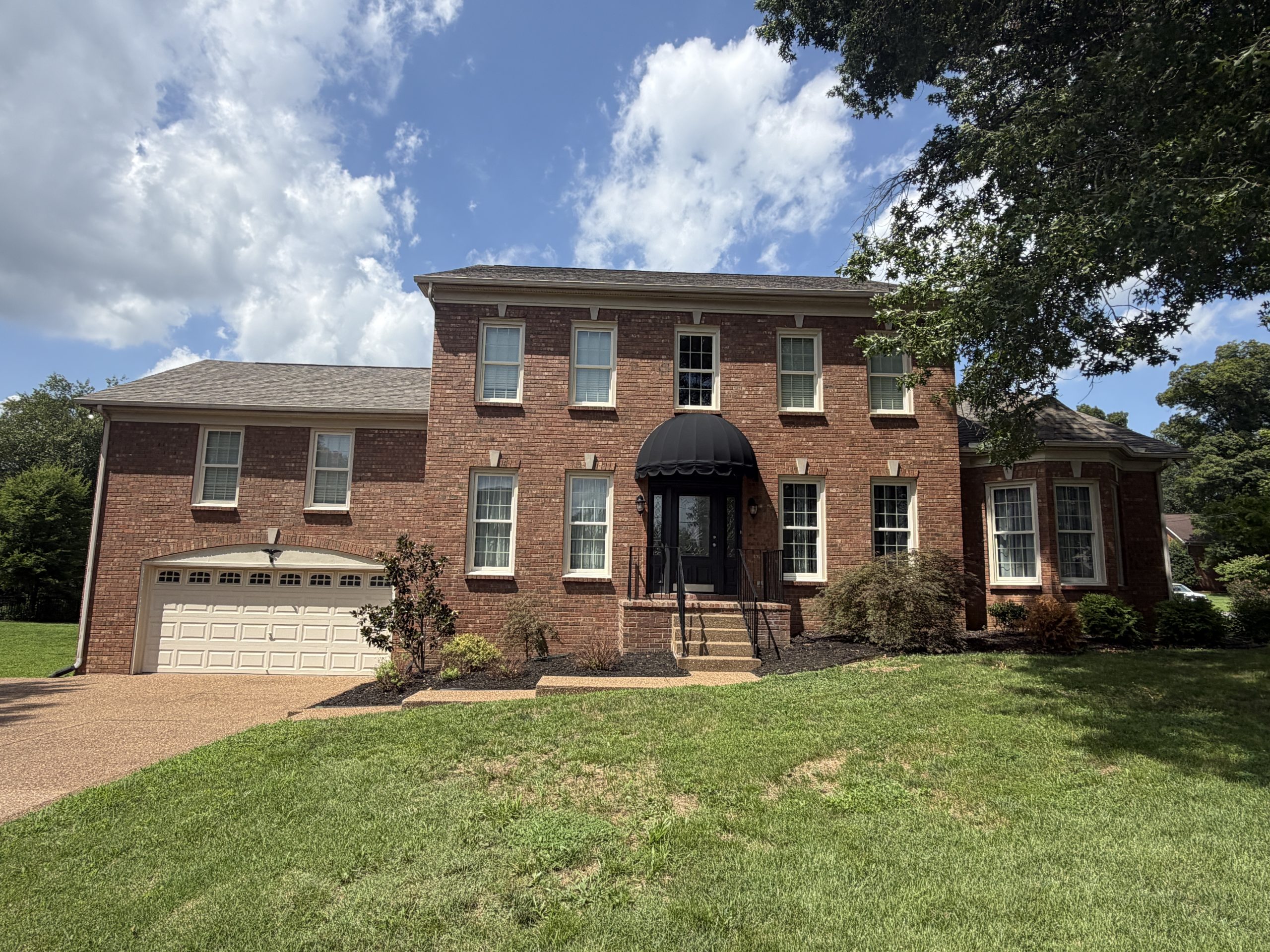 Brick two-story suburban house with a black arched entry canopy, white-framed windows, and a white garage door atop a manicured lawn.