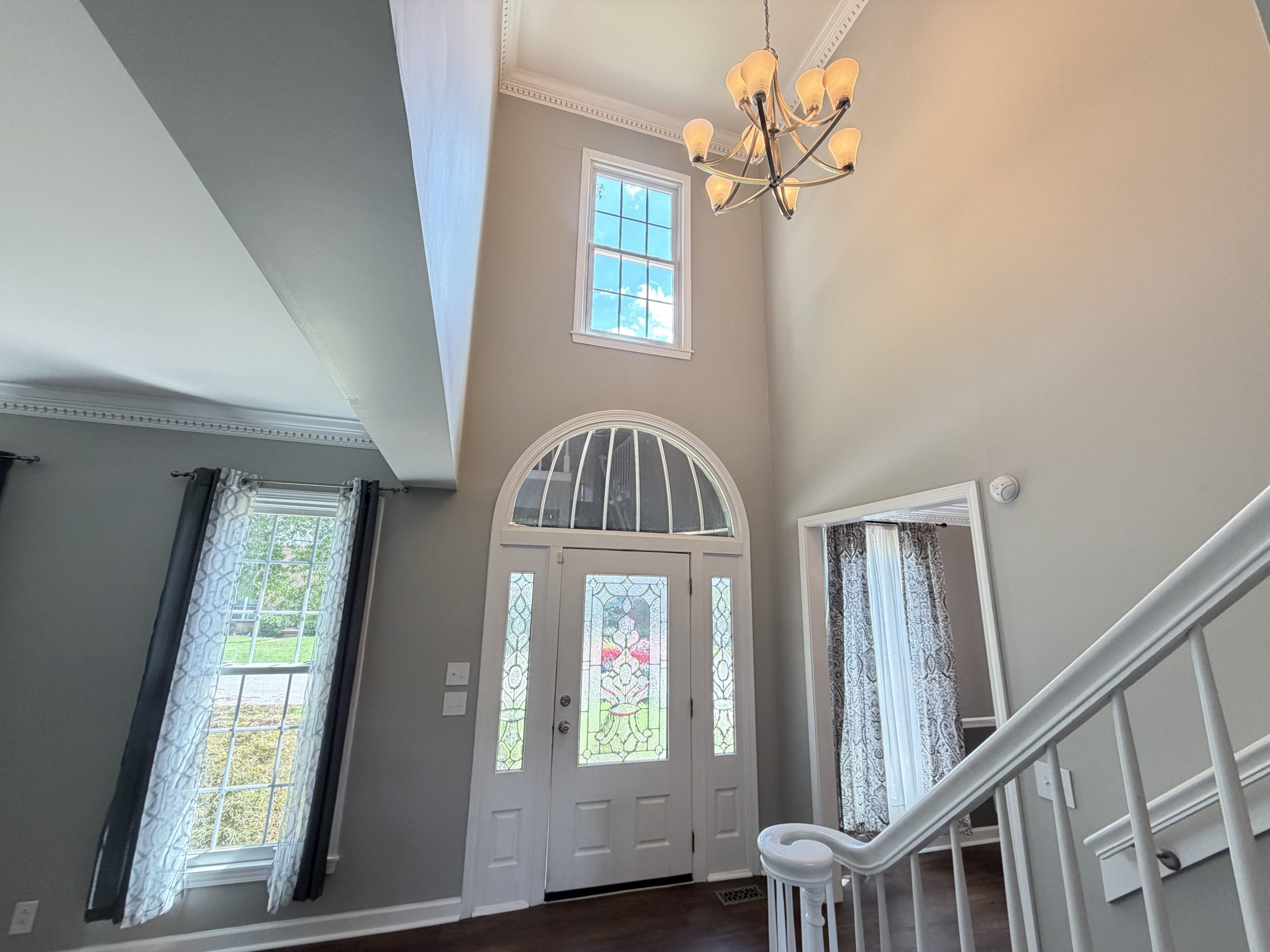 Entry foyer with white front door featuring decorative stained-glass panels and sidelights, chandelier overhead.”,