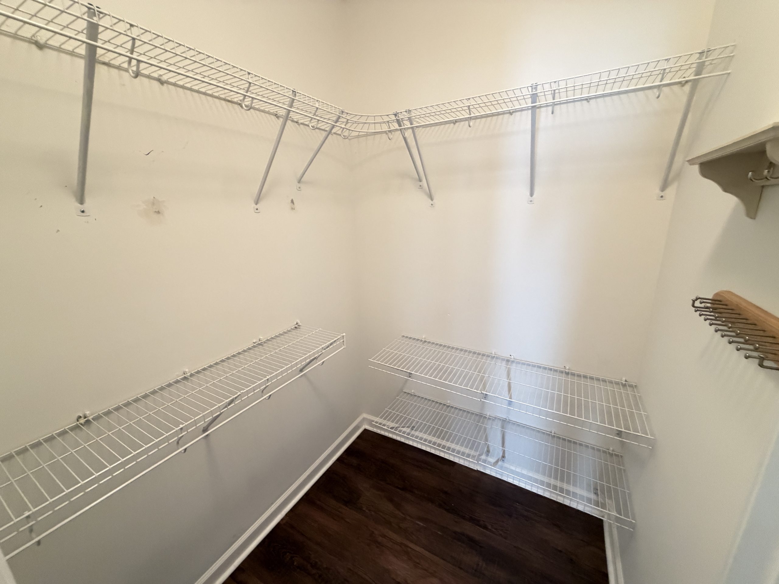 Empty walk-in closet with white wire shelves and dark wood floor, awaiting storage.