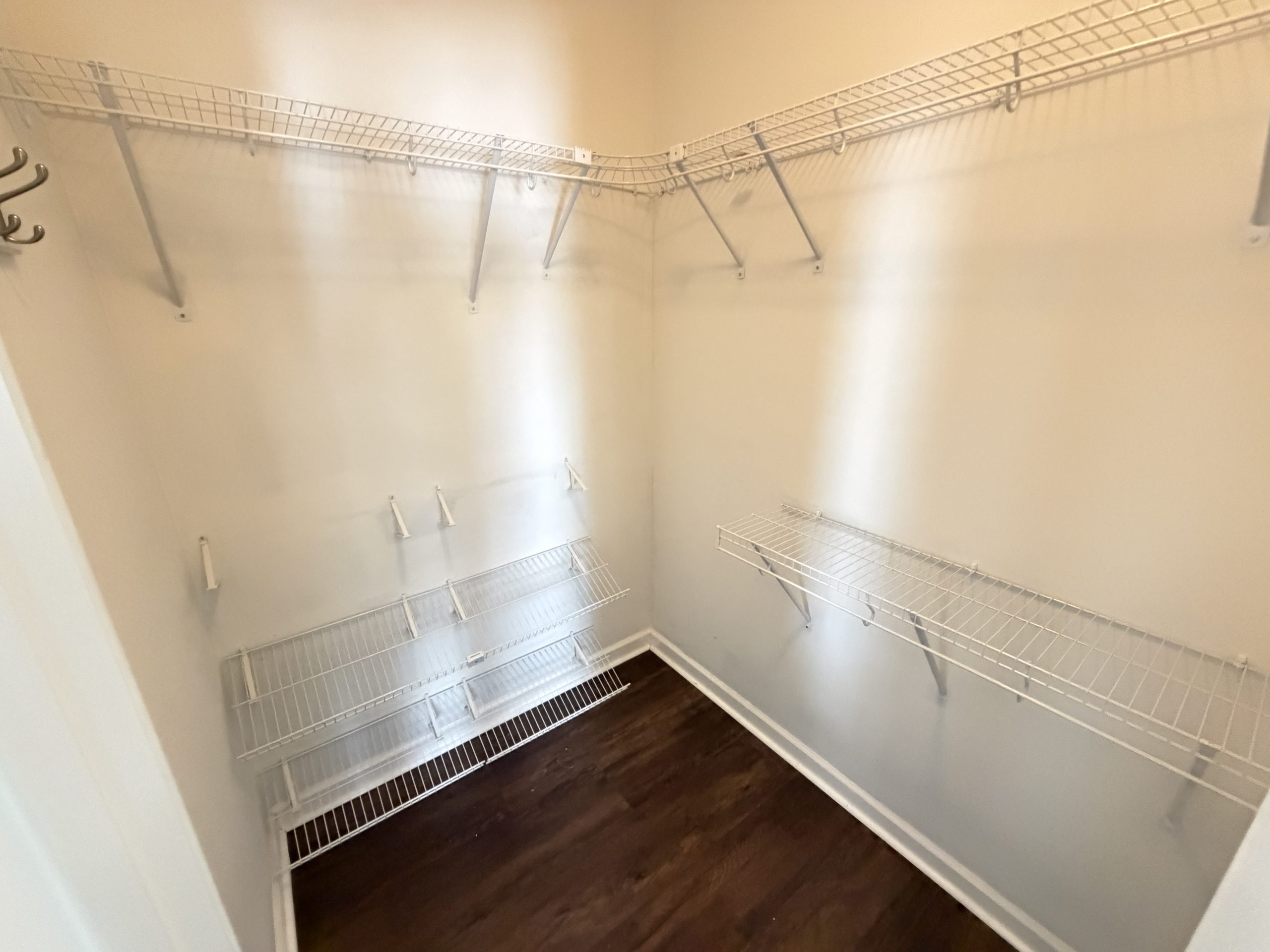 Empty walk-in closet with white wire shelves and hanging rods along two walls, and dark wood flooring.