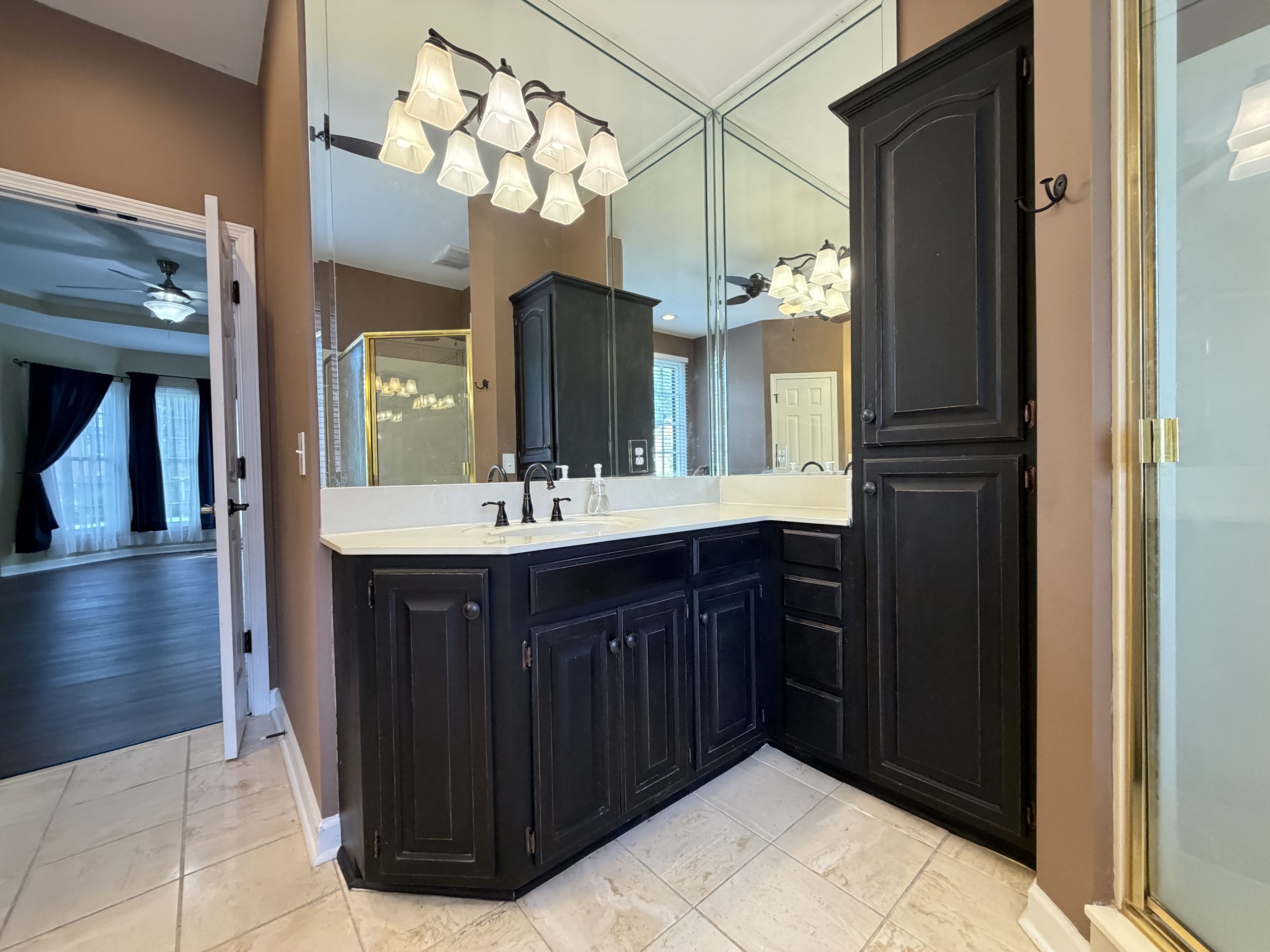 Bathroom vanity with dark wood cabinets, white counter, and a multi-light chandelier reflected in mirrored walls.