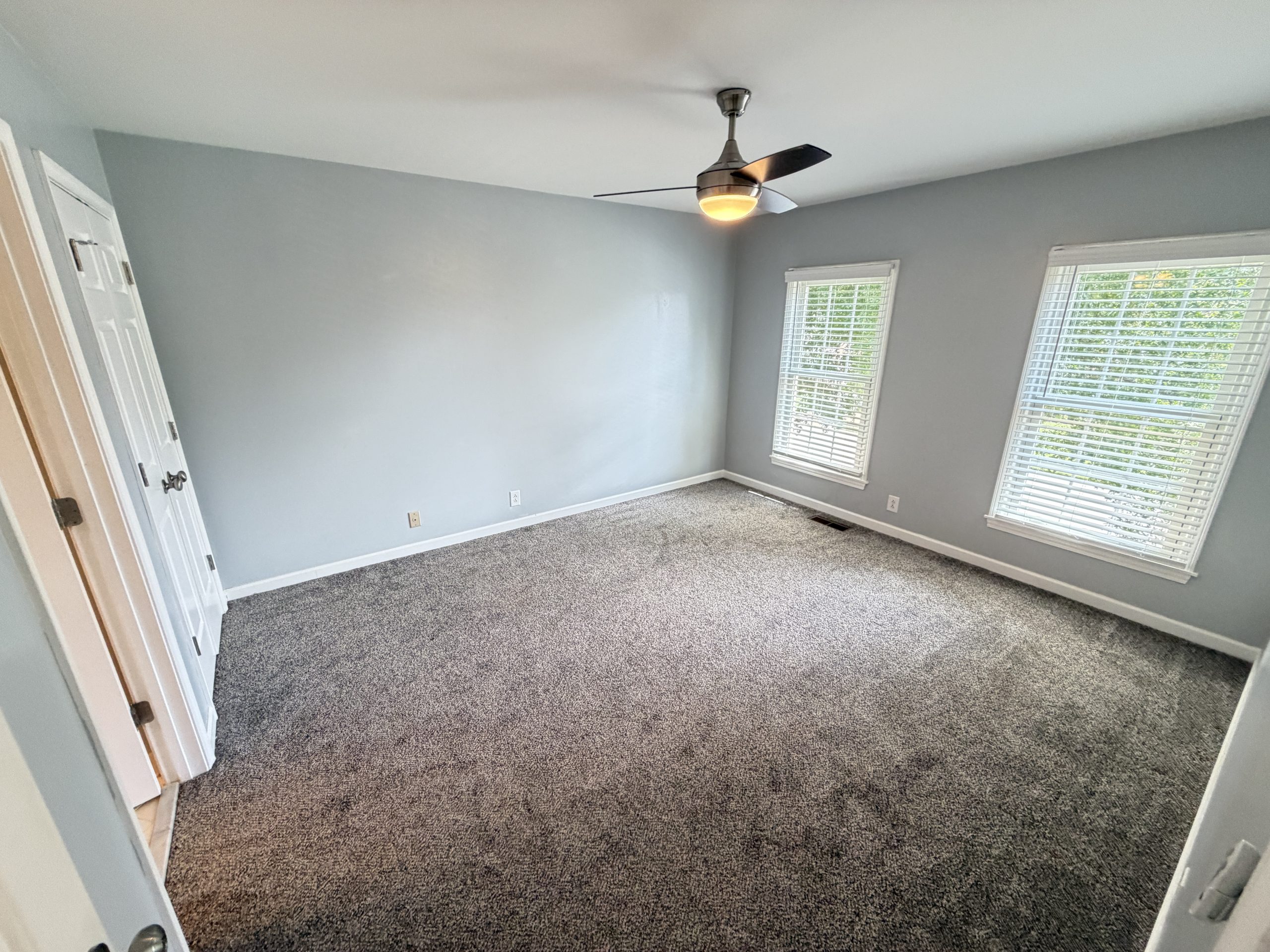 Empty bedroom with light gray walls, beige carpet, and a ceiling fan with light in the center of the room