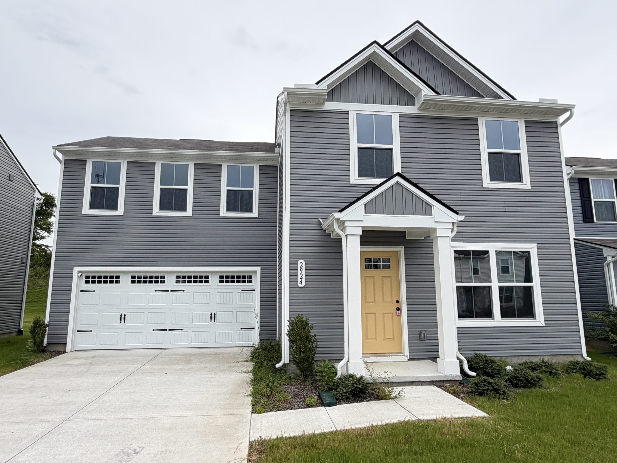 Two-story gray house with white trim, yellow front door, and attached garage; a modern suburban home exterior.