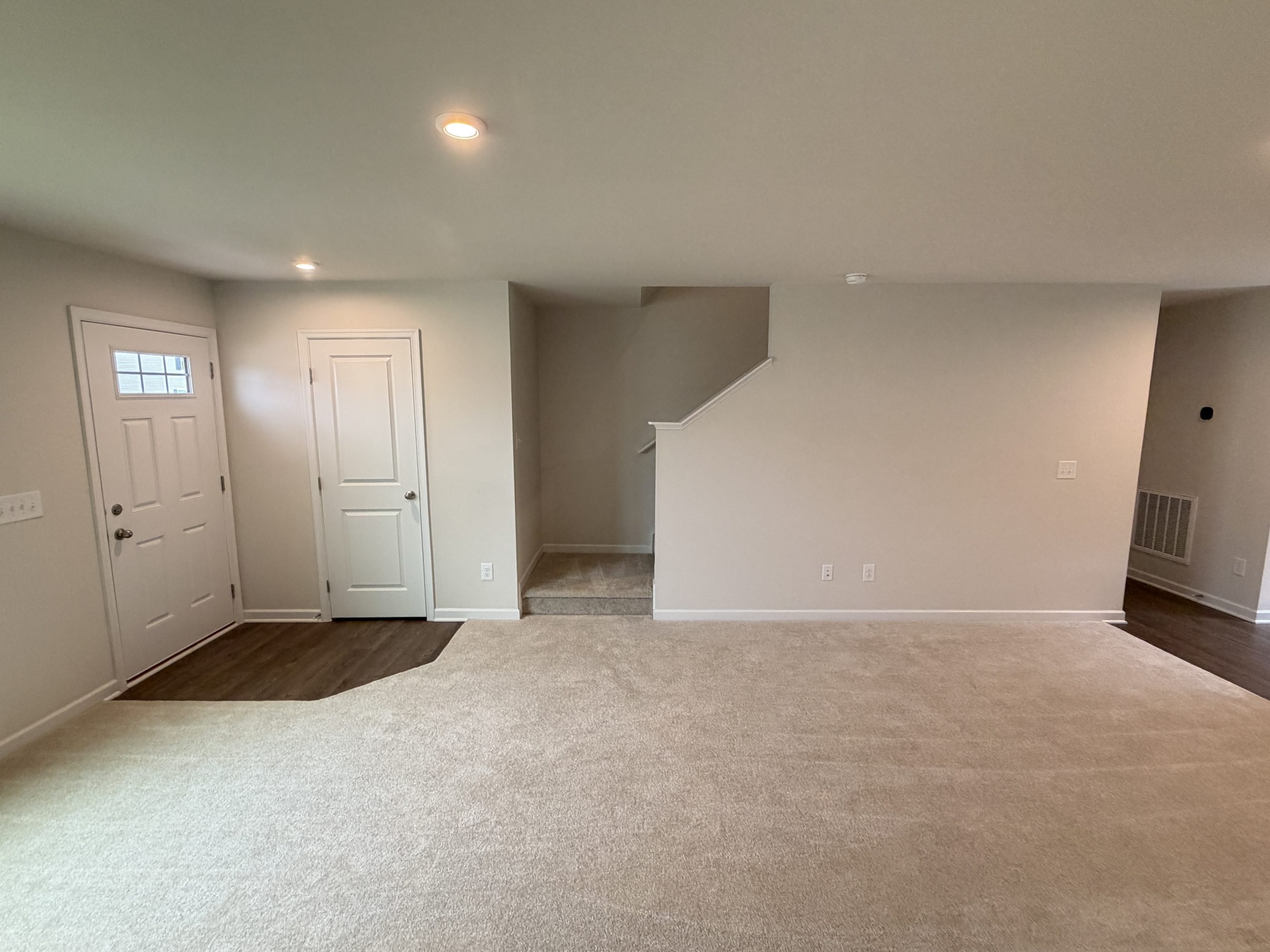Basement living area with beige walls, carpeted floor, two white doors on the left, and a short staircase in the center.
