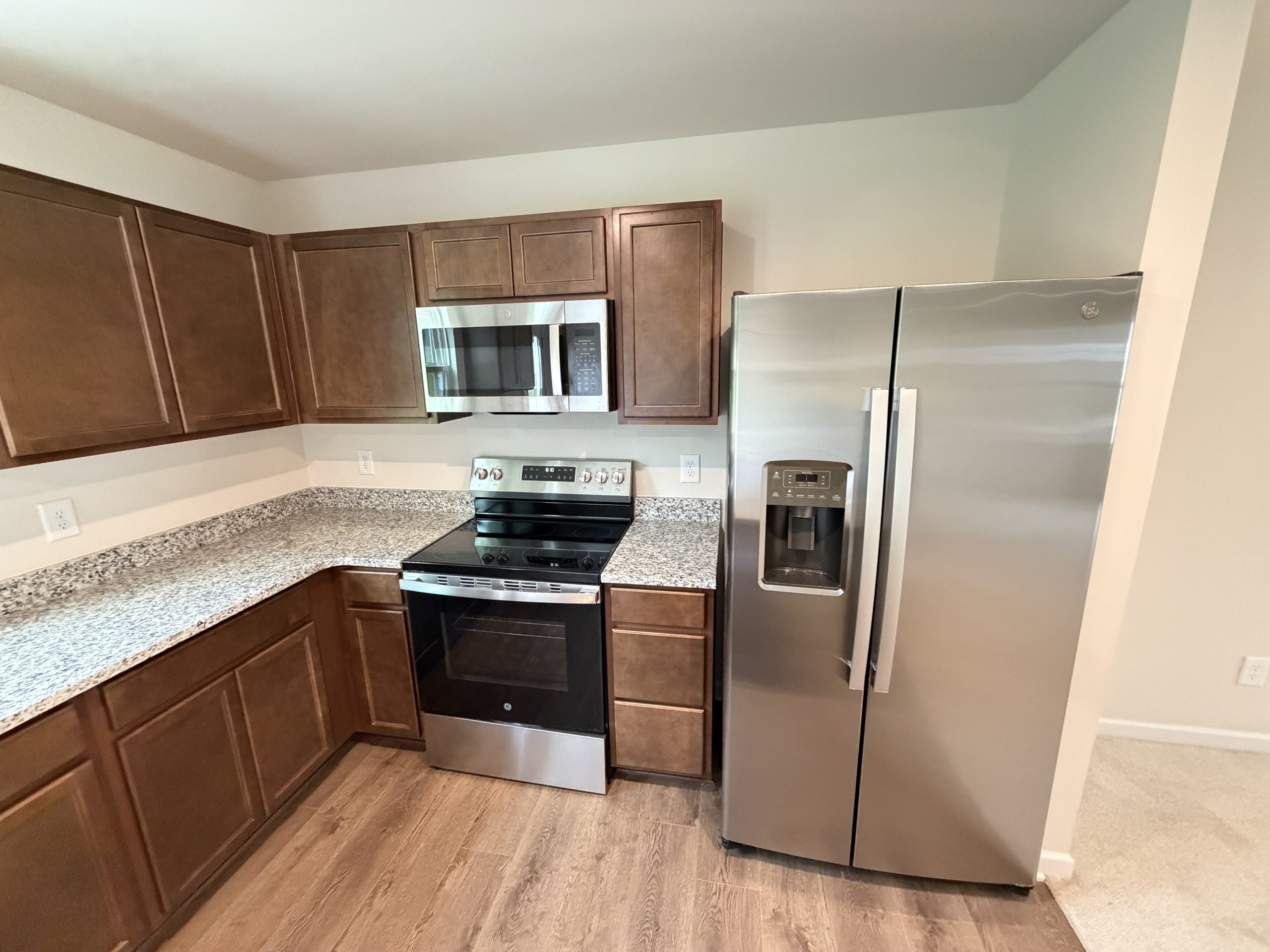 Modern kitchen with dark wood cabinets, granite countertops, and stainless steel appliances (microwave above stove, fridge to the right).