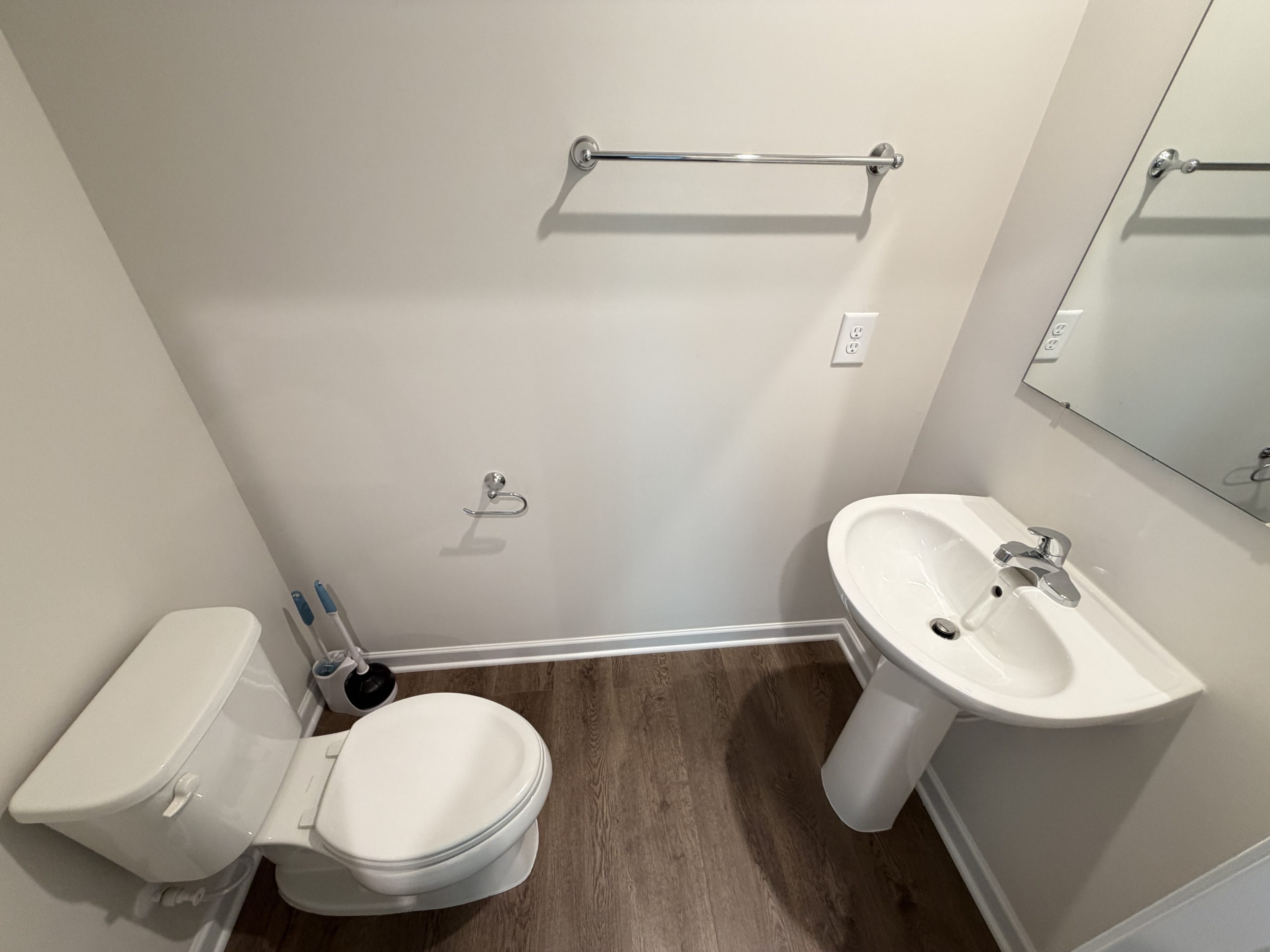 Compact bathroom with a white toilet, pedestal sink, and chrome towel bar on light walls.