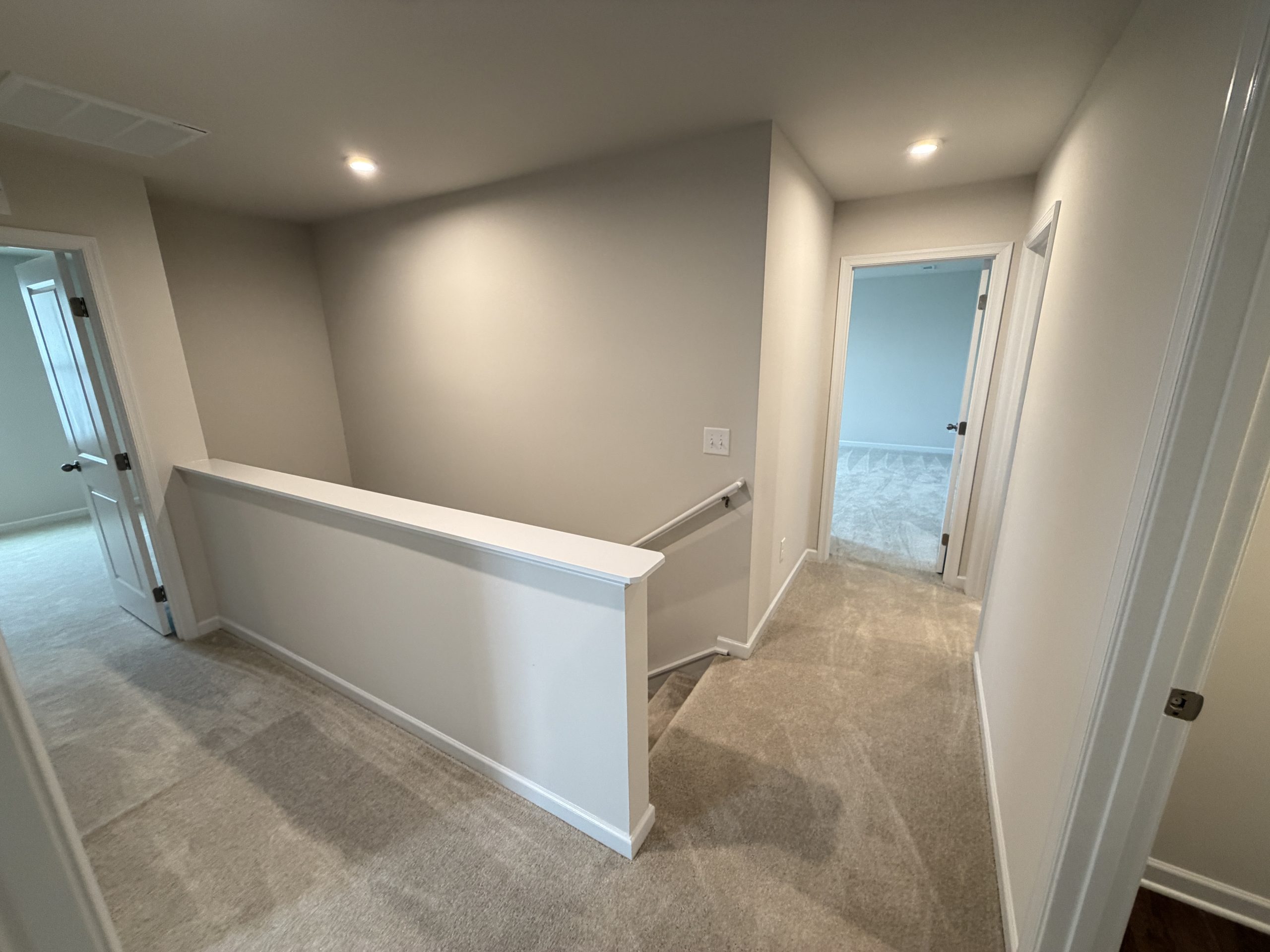 Upper hallway with beige carpet, gray walls, white railing, and multiple white doors on either side, leading to adjacent rooms.