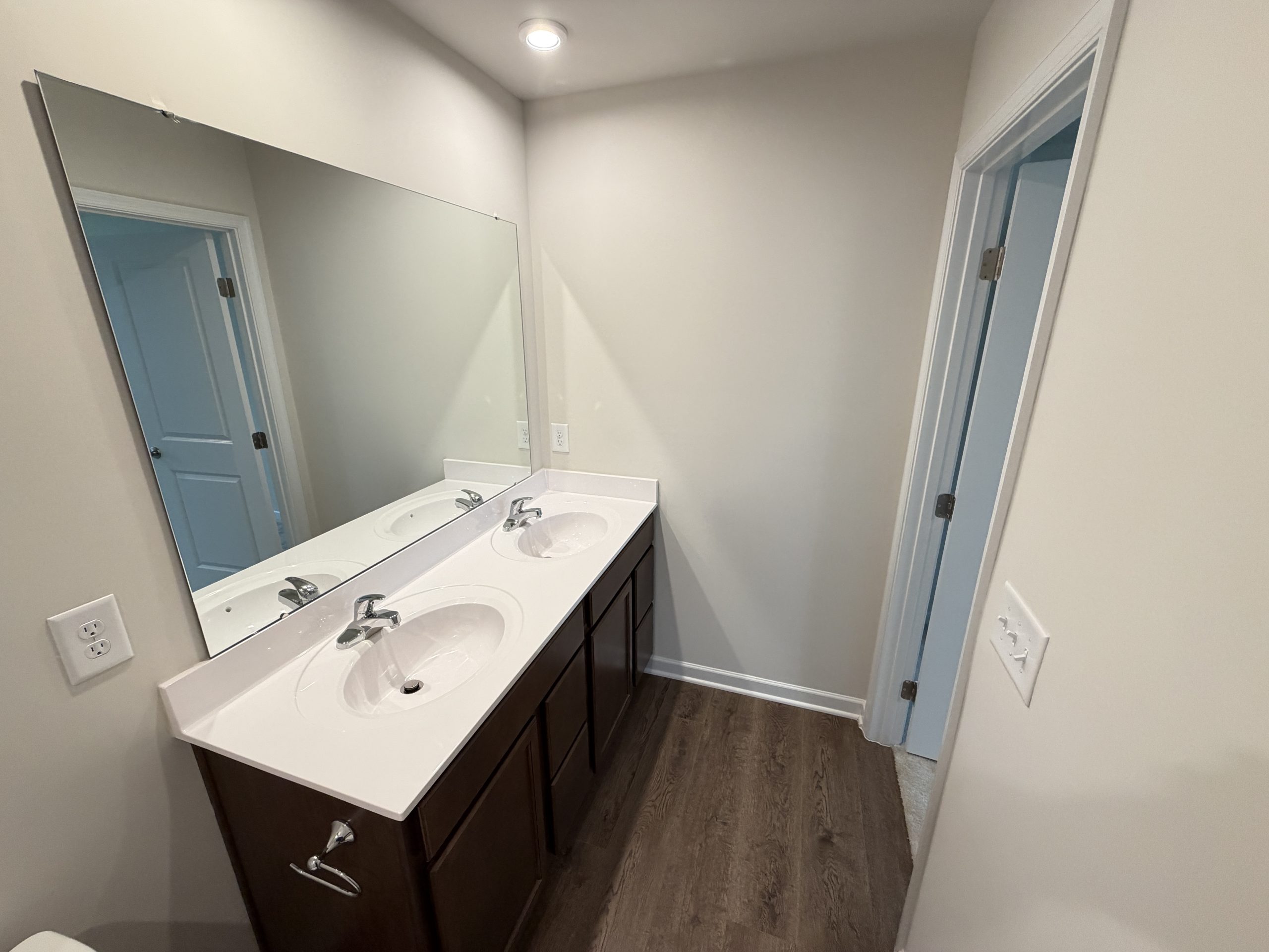 Bathroom with a double-sink vanity, dark wood cabinets, and a large mirror reflecting a doorway.