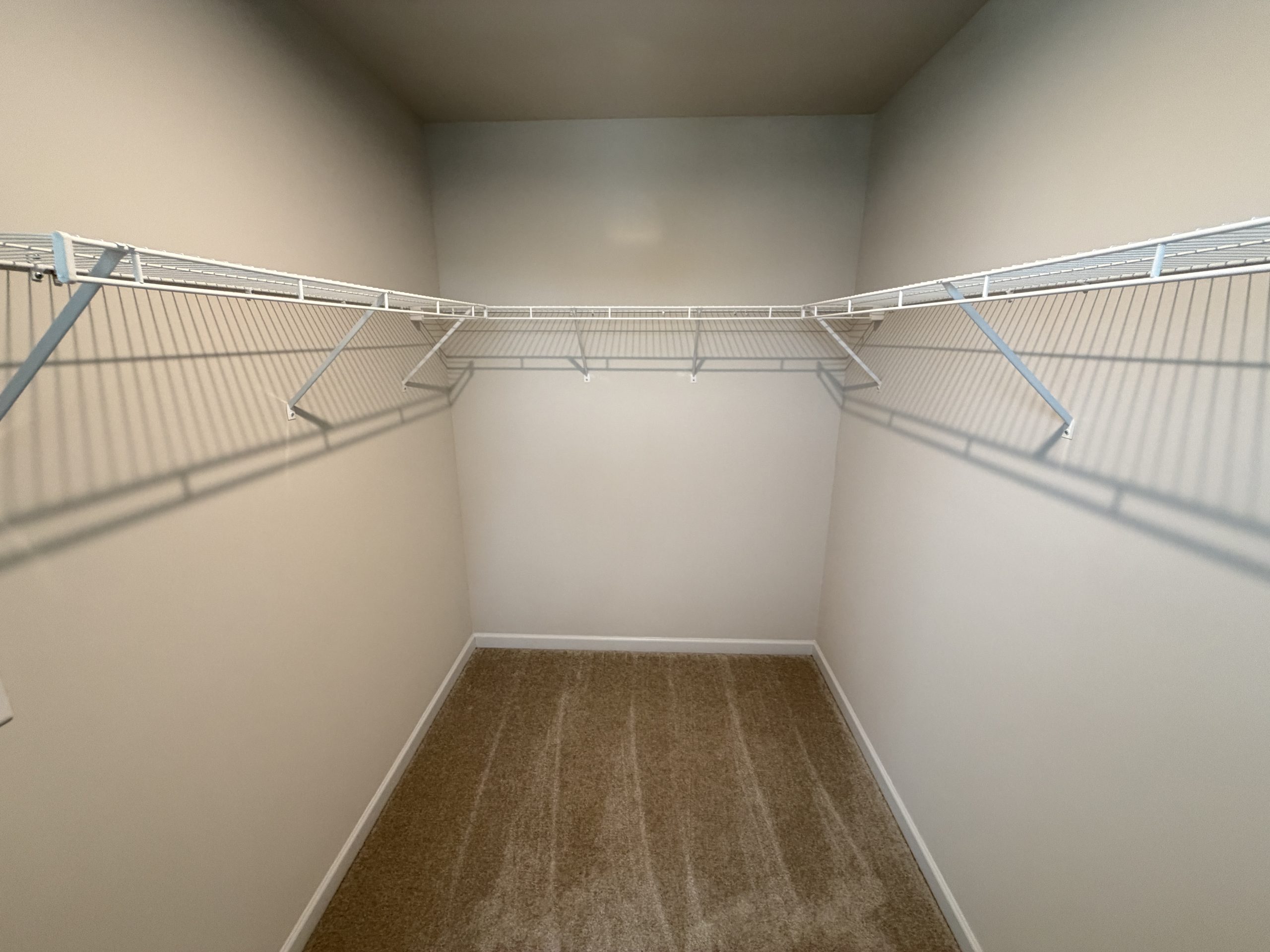 Empty walk-in closet with white wire shelving along both walls and beige walls